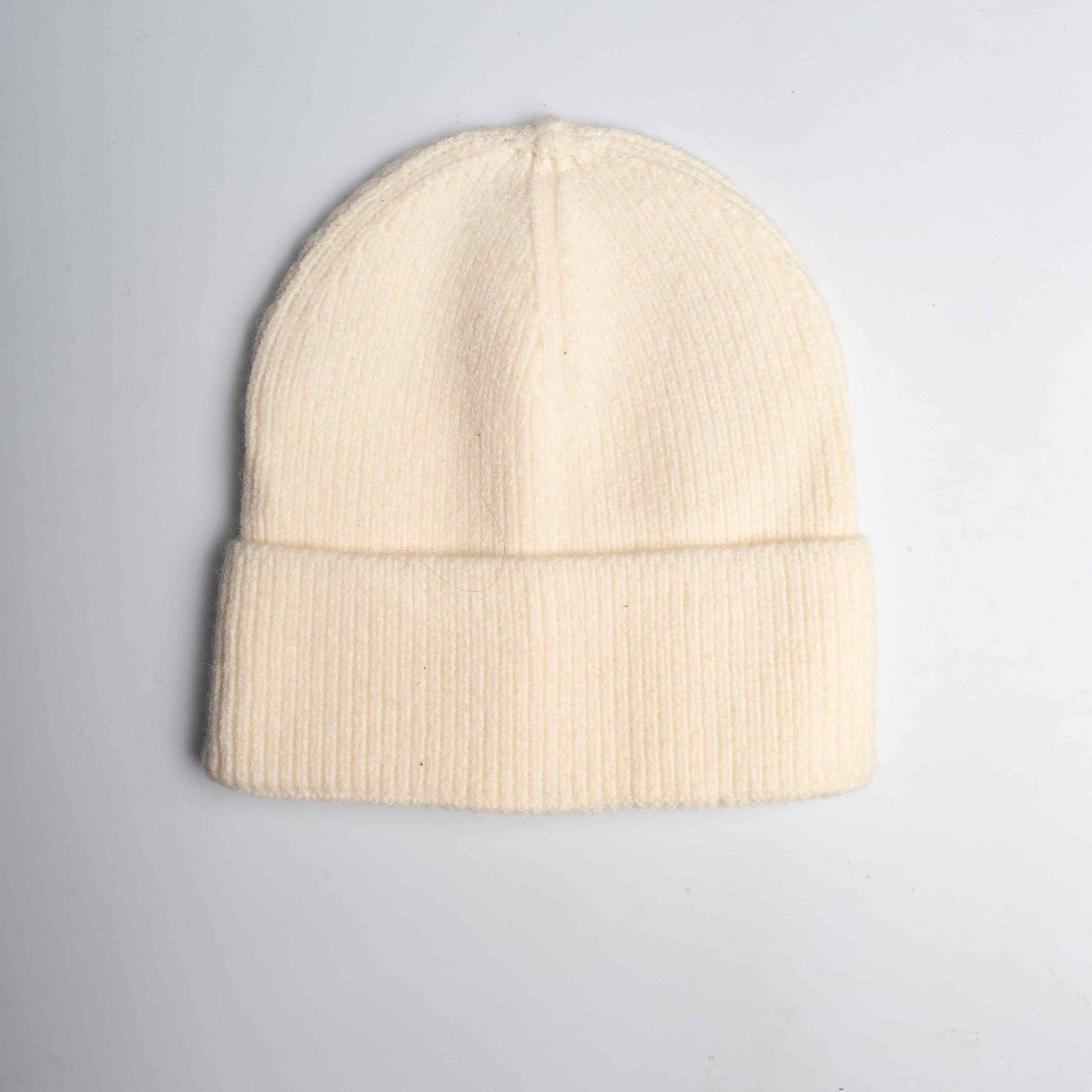 Close-up of a white cozy wool knitted winter cap in a classic design, showcasing its textured pattern and soft, warm material, placed on a neutral background.